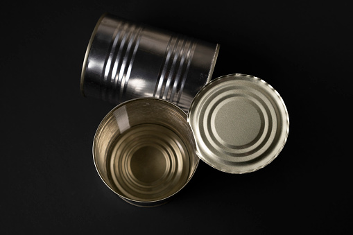 High angle view of metal tins of food of different sizes, colors and shapes shot on dark wooden table. High resolution 42Mp studio digital capture taken with Sony A7rII and Sony FE 90mm f2.8 macro G OSS lens