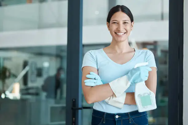 Photo of Cleaning service, portrait and cleaner in an office with spray bottle of disinfectant, bleach or detergent. Happy, smile and young female worker with gloves and soap liquid done washing glass windows