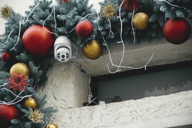 Stylish safety camera and christmas baubles on fir branches on building exterior. Modern christmas decor and security equipment in city street. Winter holidays in Europe. stock photo