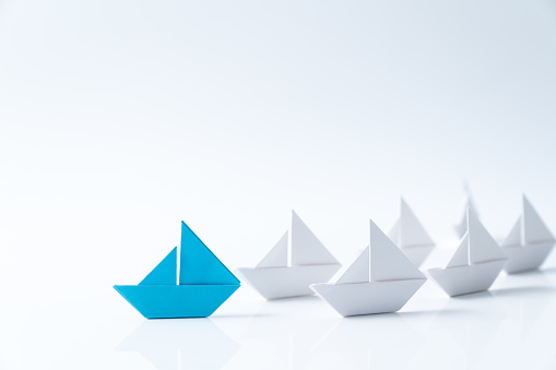 Leadership or leader concept using a blue paper ship leading among white ships