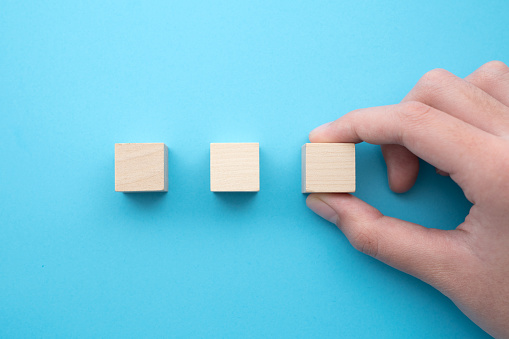 Hand holding a row of three blank wooden cubes on a blue background in a conceptual image, ready for your text.