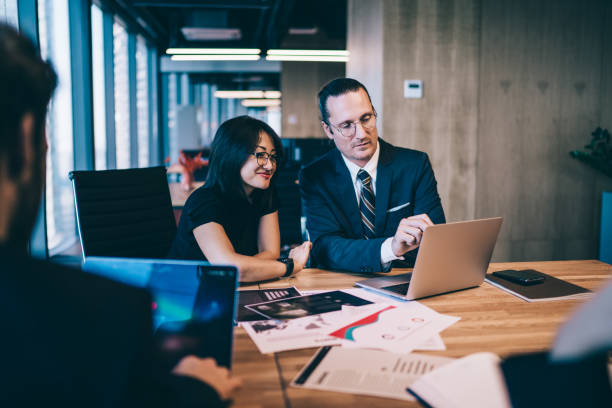 Successful multicultural male and female skilled professionals collaborating on project using 4g wireless internet on laptop computer during work time in conference room, concept of business