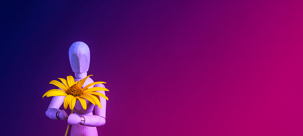 Wooden mannequin holding a yellow flower. Blue - purple color gradient background, space for copy.