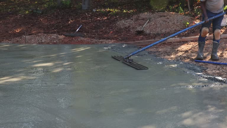 Mason worker leveling concrete patio floor using a long trowel