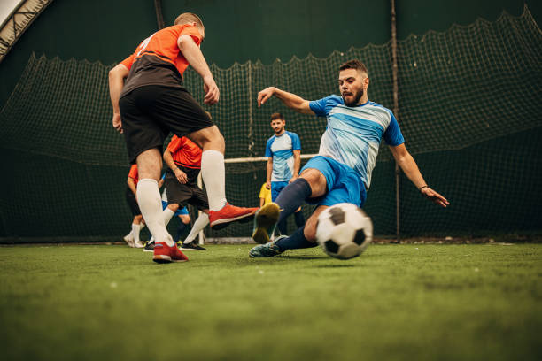 Slide tackle Group of men, male soccer players playing a match on soccer field indoors. soccer team captain stock pictures, royalty-free photos & images
