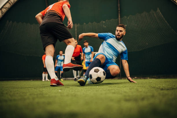 Slide tackle Group of men, male soccer players playing a match on soccer field indoors. soccer team captain stock pictures, royalty-free photos & images