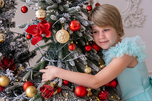 a teenage girl in a beautiful dress hugs a Christmas tree. Love, christmas and new year.
