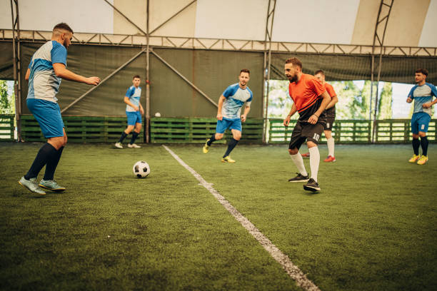 Group of men, male soccer players playing a match on soccer field indoors.