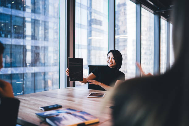 Successful Chinese female holding paper financial report for analyzing during brainstorming meeting for communicate with colleagues in modern office,concept of business investment and entrepreneurship