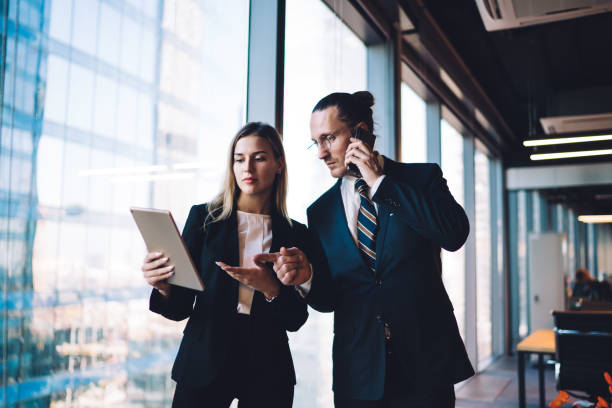istock Caucasian boss reading financial news on modern touch pad while communicating with corporate investor via cellphone, formally dressed colleagues using technology with 4g internet in office interior 1440061904