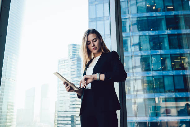 istock Confident caucasian female manager checking notification on wearable smartwatch with touchscreen and apps standing in office, millennial business woman in elegant formal wear using modern gadgets 1440061946
