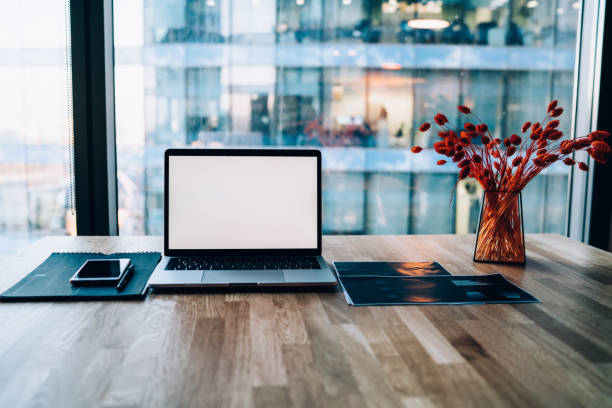 istock Image of open modern laptop computer with blank screen on wooden table in office interior connected to wireless internet, advanced equipment on working space for job with stationery and papers 1440062588