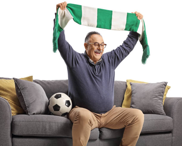 istock Mature man sitting on a sofa and cheering with a scarf 1440062844
