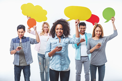Young people of different nationalities with speech bubbles are using smartphones and smiling, isolated on white background