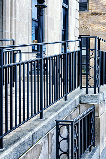 Close-up detail of a wrought iron fence and railing surrounding an elevated pedestrian walkway entrance ramp on a public city building in Rochester, New York.