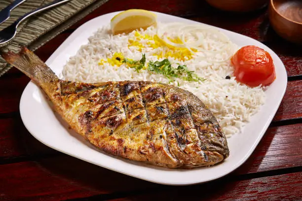 Photo of Grilled Whole Sea-bream with rice, tomato and lemon served in dish isolated on table side view of middle east food