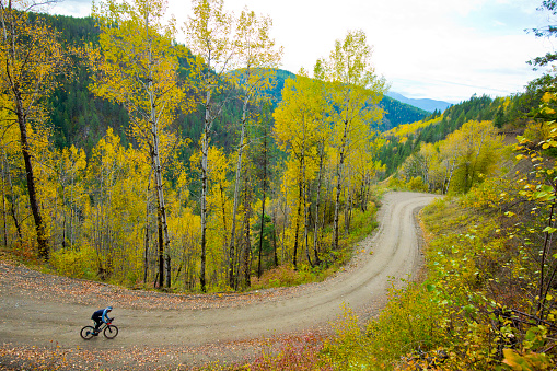 A man rides his gravel bicycle down a winding, gravel road in the mountains of British Columbia, Canada. Gravel bicycles are similar to road bicycles but have oversized tires for riding on rough terrain.