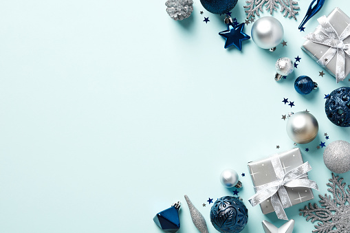 Elegant Christmas background with blue and silver decorations and gift boxes on light blue table. Flat lay, top view, copy space.