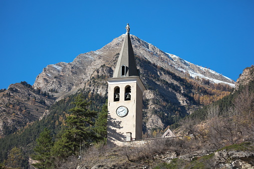 At the top of the campanile roof and with an optical illusion at the top of Pointe Fine 2581m.\n\nOn its rocky outcrop, the campanile dominates the village of Jausiers, a village in the Alpes-de-Haute-Provence located near Barcelonnette at the gates of the Hautes Vallées de l'Ubaye. Many cyclists frequent this charming village on sunny days to climb the various surrounding passes (Col de la Bonette 2715m, Col de la Cayolle 2324m, Col d'Allos 2250m, Col de Vars 2108 or Col de Larche 1991m)