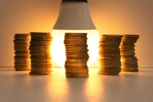 istock Energy saving lamp with coins Cost, efficiency and energy saving concept. 1440073533