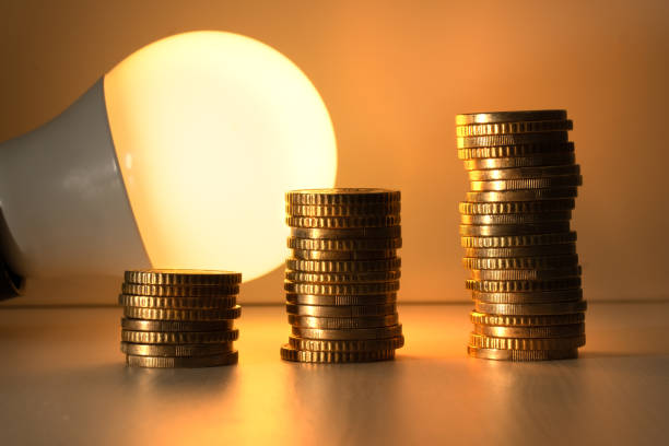 istock Energy saving lamp with coins Cost, efficiency and energy saving concept. 1440073576