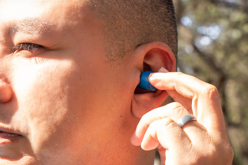 A Hispanic man puts a blue earbud in his ear