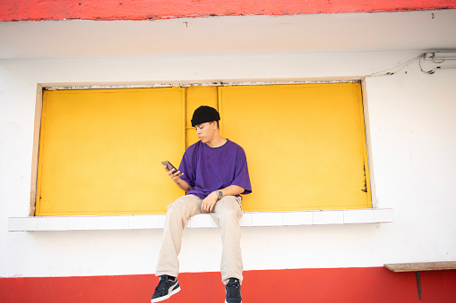 Portrait of a young Mexican man using mobile phone. He is wearing purple shirt on a colorfull background