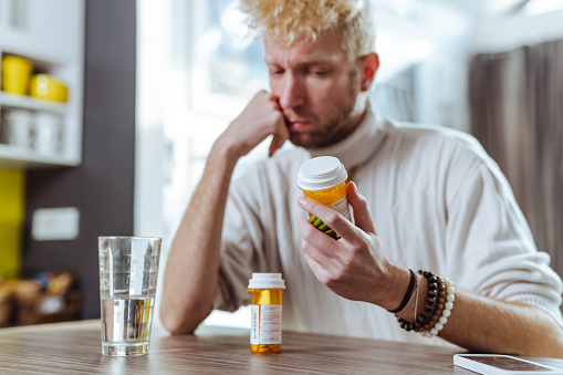 A man is sitting and holding head in his hands while thinking and looking at the pill bottles
