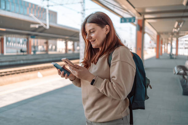 istock Happy young woman waiting on station platform with backpack on background train using smart phone. Railroad transport concept. Traveler 1440081297
