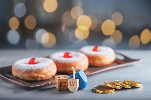 Hanukkah concept with sufganiyah, wooden dreidels,  chocolate coins and bright light in the background