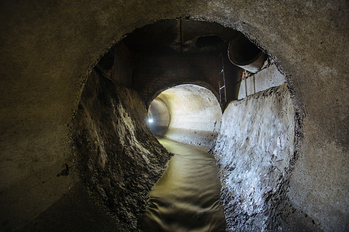 Inside underground urban sewer system. Sewage flowing in round sewer pipe