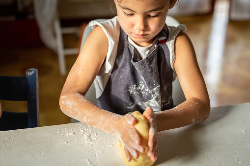 close up of child hands kneading the dough at white table