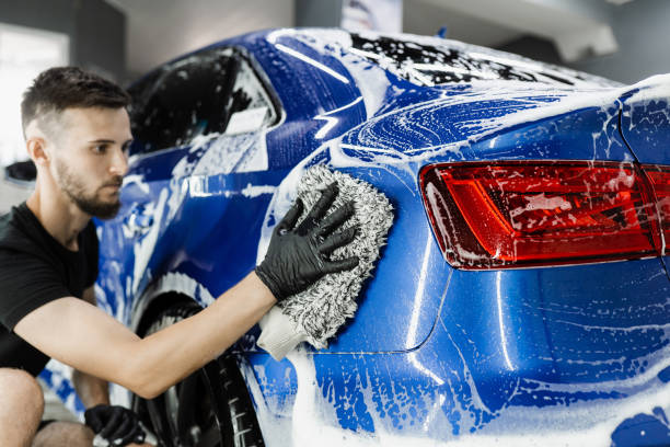 istock Car washer doing manual foam washing in auto detailing service. Hand washing with microfiber glove with foam car body in garage. 1440093115