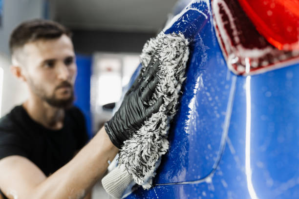 istock Car washer doing manual foam washing in auto detailing service. Hand washing with microfiber glove with foam car body in garage. 1440093117