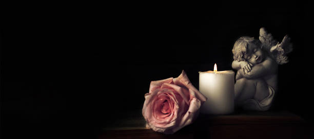 Angel, funeral flower and candle on black background with copy space