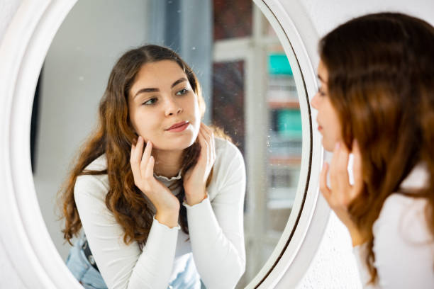 istock Young woman looking at face in mirror 1440098625