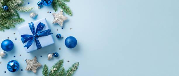 concept de noël. photo de dessus de la grande boîte de cadeaux avec ruban nœud boules bleues et blanches ornements d’étoile d’argent branches de pin dans le givre et confettis sur fond bleu clair isolé avec copyspace - christmas christmas ornament blue decoration photos et images de collection