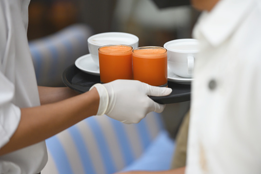 Close-up of waitress bringing coffee and carrot juice, wearing protective gloves