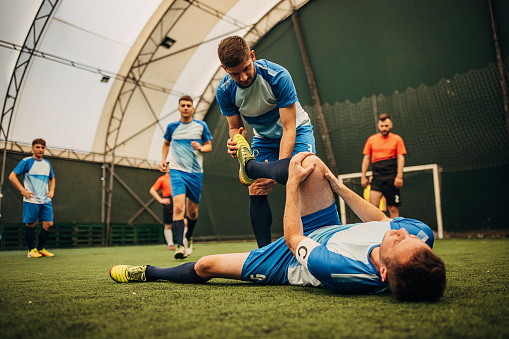 Group of men, male soccer player lying on grass injured in soccer match.