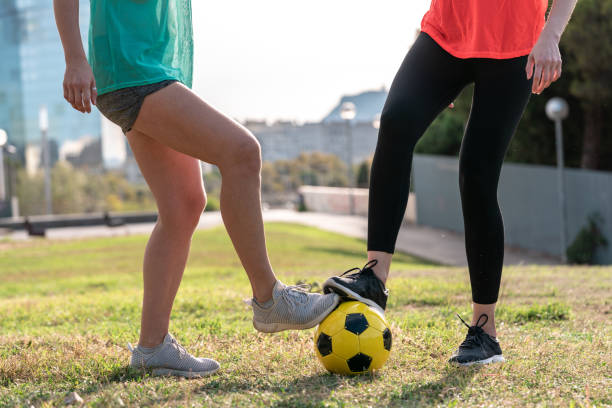アマチュアチームでサッカーやヨーロッパのサッカーをするために訓練している2人の30代の女性。黄色いボール、緑の芝生の運動場。 - 35 40 years women female smiling ストックフォトと画像