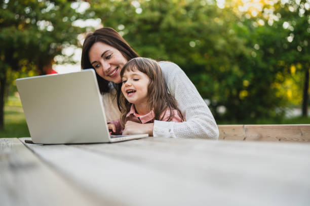 Mother working on laptop while having rest and relax in a public park with daughter.