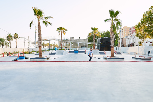 View of skate park with palm trees. Unrecognizable tricker riding towards camera.