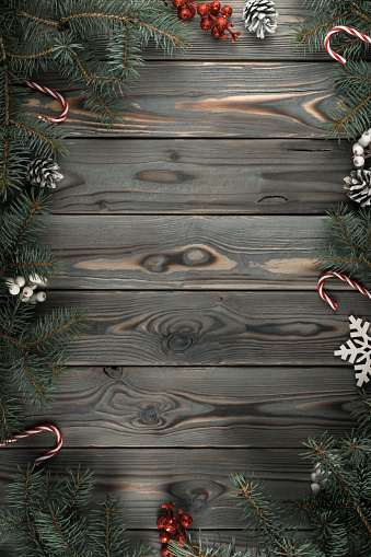 Vertical composition frame of Xmas decoration greeting card with empty wooden space. Cones, lollipops, candies and evergreen tree branches as border. Happy new year, merry christmas eve. Top view