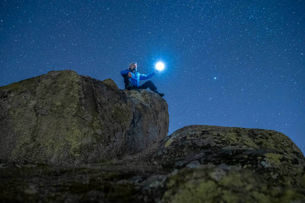 istock Man with light at night standing on a rock under starry sky. 1440110204