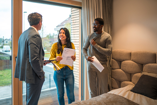 Young Hispanic woman and African American male husband buying a new studio apartment together. They are indoors in a meeting with a mature caucasian real estate agent.