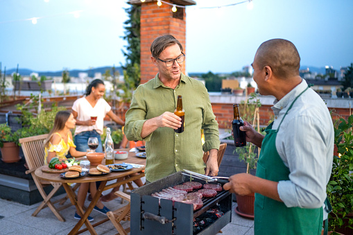 Men having a beer and grilling a meat steak while women having conversation at the rooftop dinner party