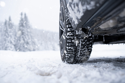 Low angle shot of snow covered tyre on snowy road.