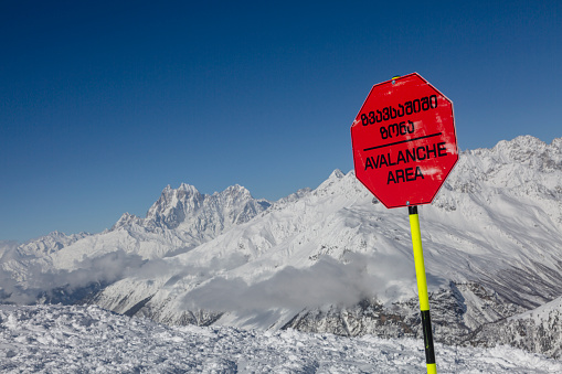 An Avalanche terrain near a mountain slope. The inscription on the red sign: Avalanche caution