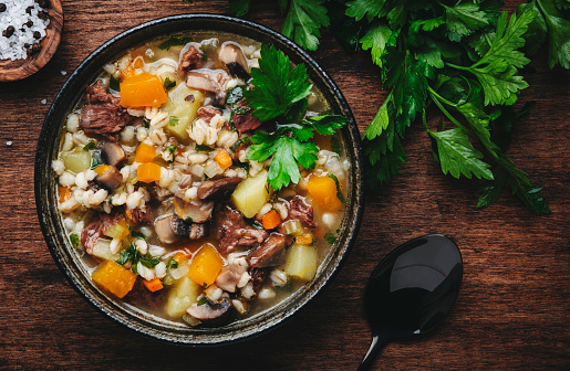 Autumn food. Warming soup with pumpkin, mushrooms, vegetables, beef and barley. Rustic wood table background, top view