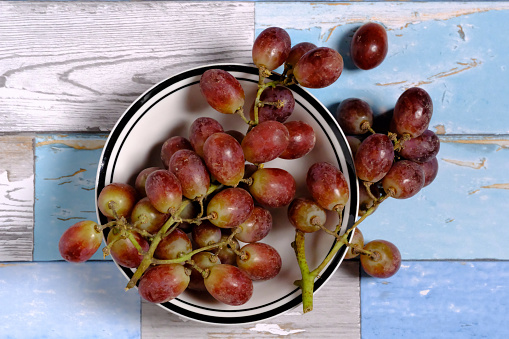 Red grapes in a bowl and isolated on weathered wooden background.